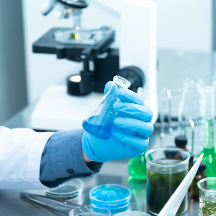 pexels-photo-2280571-2280571 Scientist in gloves analyzing blue liquid in a laboratory setting with microscope and glassware.